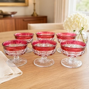 May include: A set of six glass dessert bowls featuring a deep red rim and a clear, textured base with a geometric pattern. Each bowl stands on a short, sturdy pedestal stem, showcasing a clear glass foot and a wide, shallow basin for serving.