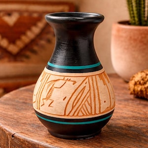 May include: A small, rounded vase featuring a matte black finish on the neck and base, accented by two horizontal turquoise stripes. The central body displays a light tan, unglazed section decorated with etched geometric and linear patterns.