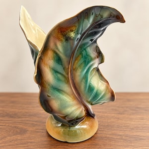 May include: A ceramic vase shaped like a large, curled leaf. The exterior features a glossy, blended glaze in shades of deep forest green, warm amber, and dark brown. The interior of the vase is a smooth, cream-colored finish with a wide opening.