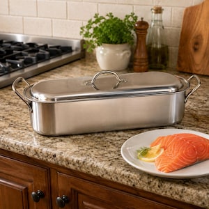 May include: A rectangular stainless steel fish poacher with a matching lid and two side handles. The polished metal vessel features a long, narrow shape designed for cooking whole fish, presented with a smooth, reflective surface finish.