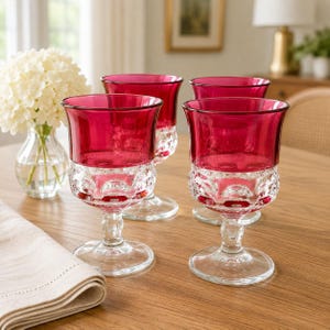 May include: A set of four wine glasses featuring deep red bowls and clear, textured glass stems and bases. The bowls have a smooth, solid red finish, while the lower sections and stems display a raised, repeating circular pattern in clear glass.