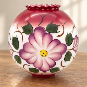 May include: A spherical glass vase with a ruffled top edge, featuring a white base with a hand-painted large purple flower at the center, green leaves, and brown vine accents, finished with a deep red gradient at the top rim of the object.