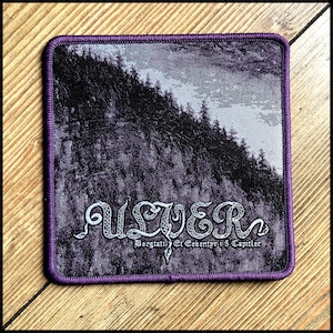 Könnte beinhalten: Quadratischer Aufnäher mit lila Rand. Er zeigt eine Berglandschaft in Lila- und Grautönen. Das Wort "ULVER" ist weiß gestickt, mit zusätzlichem Text darunter. Wahrscheinlich ein Band- oder Musikmerchandise-Artikel.