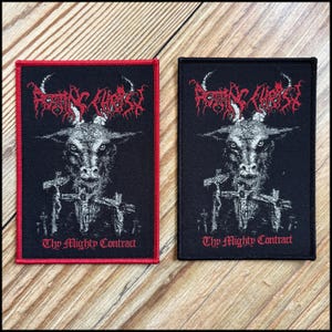 May include: Two rectangular black patches with red and white text and imagery. The patches feature a goat-like creature with a cross and the words "Thy Mighty Contract". One patch has a red border.