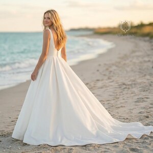 May include: A floor-length white sleeveless wedding dress with a deep scoop back, a full A-line skirt, and a vertical row of small fabric-covered buttons running down the center of the back bodice, extending into the skirt's train.