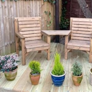 Peut inclure: Ensemble de mobilier de jardin en bois comprenant deux chaises et une petite table. Les chaises et la table sont en bois clair. Diverses plantes en pot, dont des plantes &agrave; fleurs et de petits conif&egrave;res, sont dispos&eacute;es sur la terrasse en bois.
