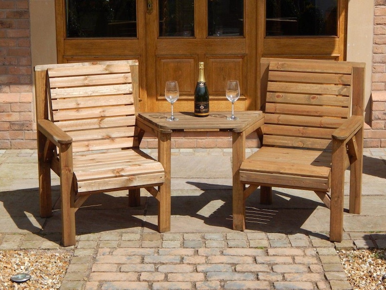 Peut inclure: Deux chaises de jardin en bois et une petite table. Les chaises ont des dossiers &agrave; lattes et des accoudoirs. Une bouteille de champagne et deux verres &agrave; vin sont sur la table. Le mobilier est en bois clair.