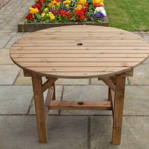 May include: A circular wooden garden table with a slatted top and four legs. The table is constructed from light-coloured wood and features a central hole. The table has a diameter of approximately 91 cm, suitable for outdoor use.