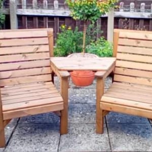 Peut inclure: Deux chaises de jardin en bois avec une petite table centrale. Les chaises et la table sont en bois brun clair et pr&eacute;sentent un design &agrave; lattes. Les chaises ont des accoudoirs. La sc&egrave;ne se d&eacute;roule sur un patio avec des plantes en pot en arri&egrave;re-plan.