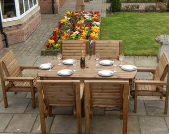 May include: A wooden outdoor dining set with a rectangular table and six matching chairs. The table is set with plates, wine glasses, and a bottle of champagne. The set is surrounded by a garden with colorful flowers.