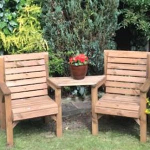 Peut inclure: Deux chaises de jardin en bois et une petite table. Les chaises ont des dossiers &agrave; lattes et des accoudoirs. Un petit pot de fleurs marron est pos&eacute; sur la table. Le mobilier est en bois brun clair, sur de l'herbe.