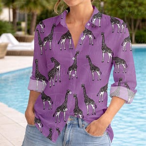 Op de afbeelding: Een paars overhemd met een herhalend patroon van zwart-witte giraffen. Het shirt met lange mouwen heeft opgerolde manchetten en een klassieke kraag. Het shirt wordt gedragen met een blauwe spijkerbroek.
