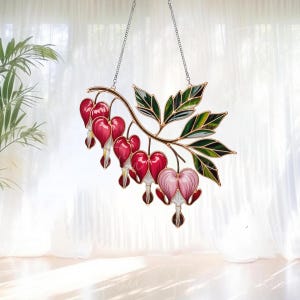 May include: A stained glass hanging decoration featuring a branch of bleeding heart flowers. The flowers are a vibrant red and pink, with a gold-colored branch and green leaves. The piece hangs from a silver chain.