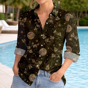 May include: Dark green button-down shirt with a celestial pattern. The shirt features a repeating design of moons, stars, and ivy leaves in shades of gold and brown. The sleeves are rolled up, revealing a lighter patterned cuff.