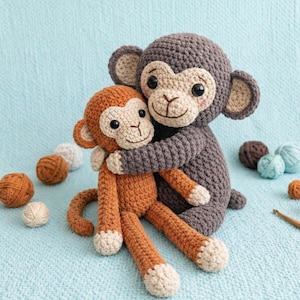 Puede incluir: Dos muñecos de mono de ganchillo, uno abrazando al otro. El mono más grande es gris y el más pequeño es naranja. Ambos tienen caras, orejas y pies beige. El fondo es de tela azul claro, con ovillos de lana esparcidos.