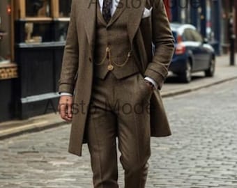 May include: A brown tweed three-piece suit with a long coat, white shirt, and patterned tie. The suit includes a vest and trousers. The person is wearing a dark cap and black dress shoes. A pocket watch chain is visible.