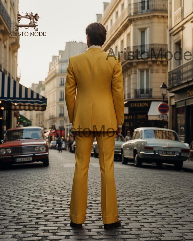 May include: A yellow suit with a tailored jacket and flared pants. The suit is worn by a person standing on a cobblestone street. The image is taken in a European city with vintage cars and buildings.