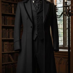 May include: A black formal suit on a mannequin. The suit comprises a long coat with a velvet collar, a waistcoat, and trousers. A black ruffled ascot is worn. The background shows a library and a candelabra.