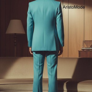 May include: A teal suit, consisting of a blazer and flared trousers, is displayed from the back. The suit is tailored and has a classic design. The brand name "AristoMode" is visible in the background. The setting is a room with a sofa and a lamp.