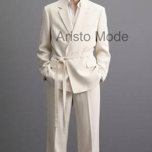 Puede incluir: Un traje color crema con una chaqueta cruzada y pantalones a juego. La chaqueta tiene cintur&oacute;n anudado y bolsillos. La imagen incluye el texto "Aristo Mode" en la parte superior izquierda y central derecha.