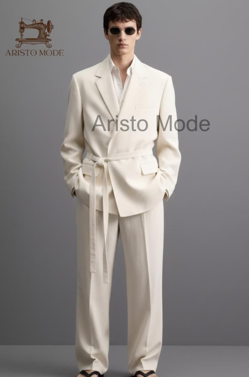 Puede incluir: Un traje color crema con una chaqueta cruzada y pantalones a juego. La chaqueta tiene cintur&oacute;n anudado y bolsillos. La imagen incluye el texto "Aristo Mode" en la parte superior izquierda y central derecha.