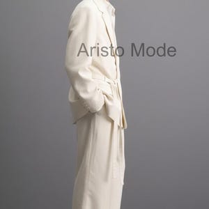 Puede incluir: Un traje color crema con pantal&oacute;n a juego. La chaqueta tiene solapas con muescas y el pantal&oacute;n es de pierna ancha. El modelo lleva gafas de sol y sandalias negras. El texto "Aristo Mode" es visible en la imagen.