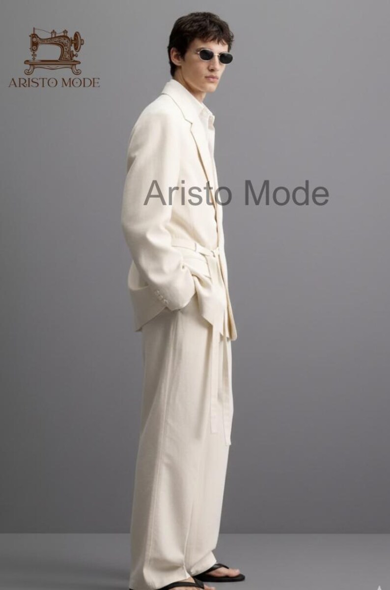 Puede incluir: Un traje color crema con pantal&oacute;n a juego. La chaqueta tiene solapas con muescas y el pantal&oacute;n es de pierna ancha. El modelo lleva gafas de sol y sandalias negras. El texto "Aristo Mode" es visible en la imagen.