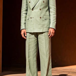 May include: A light green double-breasted suit with matching trousers. The suit features a notched lapel and brown buttons. The outfit is completed with light-colored shoes. The logo "ARISTO MODE" is visible in the top right corner.