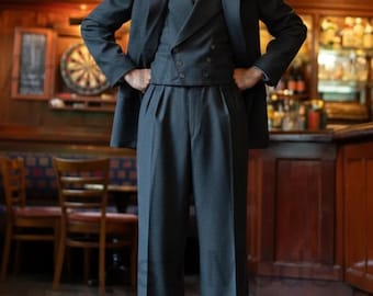 May include: A three-piece charcoal gray suit with a double-breasted vest, pleated trousers, and a matching jacket. The suit is paired with a white dress shirt and a patterned tie. The image is set in a pub setting.