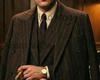 Op de afbeelding: Een bruin krijtstreep pak met een dubbelbreasted jas, vest en bijpassende broek. Het pak wordt gedragen met een wit overhemd en een stropdas met patroon. Een gouden polshorloge en een sigaar maken de look compleet.