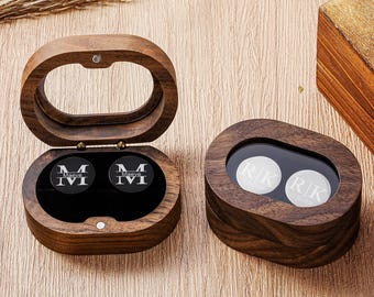May include: Two oval wooden boxes with hinged lids and glass windows. One box is open, revealing two black circular cufflinks engraved with the letter M and the name Maeve. The closed box contains two white circular cufflinks engraved with R|K.