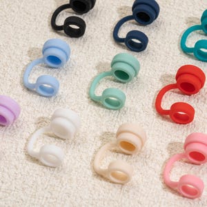 May include: A collection of colorful silicone bottle stoppers in various shades, including black, blue, green, red, pink, and white. Each stopper features a curved stem and a circular top, designed to fit snugly into a bottle opening.