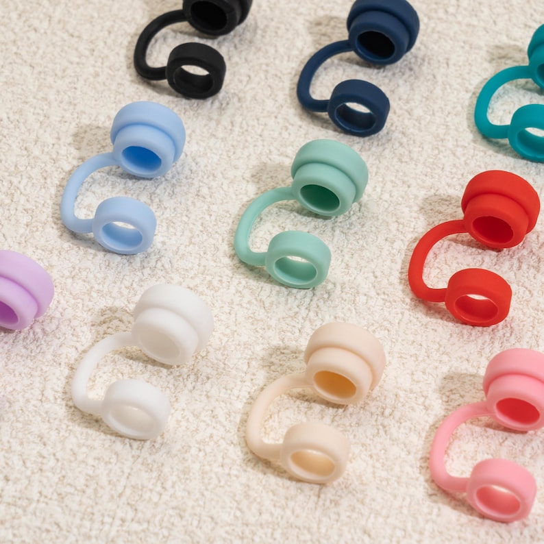 May include: A collection of colorful silicone bottle stoppers in various shades, including black, blue, green, red, pink, and white. Each stopper features a curved stem and a circular top, designed to fit snugly into a bottle opening.