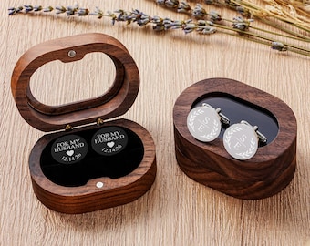 May include: Two oval dark wood boxes with hinged lids and black velvet interiors. One box is open, revealing two black circular inserts engraved with FOR MY HUSBAND, a heart, and 12.14.26. The other box is closed, displaying two silver cufflinks.