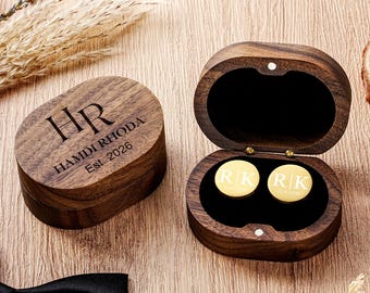 May include: A dark wood oval box engraved with HR, HAMDI RHODA, and Est. 2026, paired with an open matching box containing two round gold cufflinks featuring the initials R|K and the date 12.06.2026 on a black velvet interior lining.
