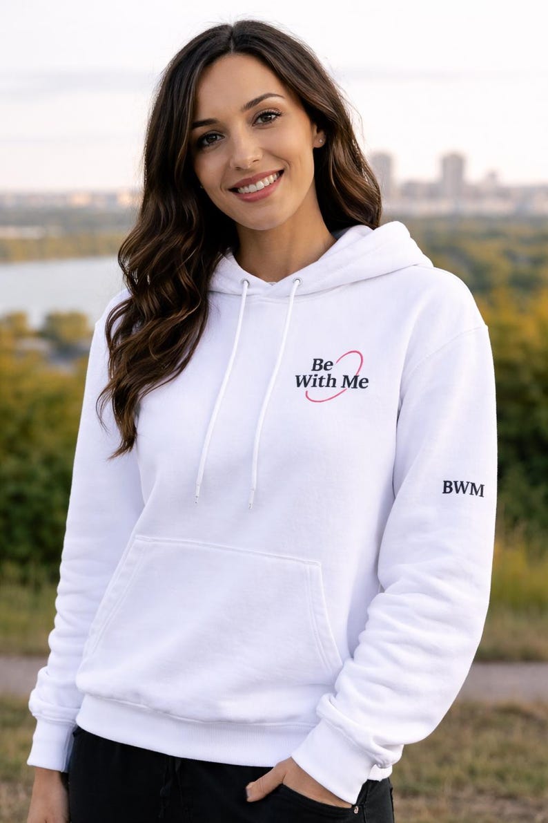 Puede incluir: Sudadera con capucha blanca con bolsillo delantero y cord&oacute;n. El texto "Be With Me" est&aacute; impreso en el pecho con un dise&ntilde;o de coraz&oacute;n rosa. Las letras "BWM" est&aacute;n en la manga.