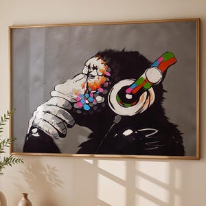 May include: A framed artwork featuring a chimpanzee wearing headphones. The chimp is depicted in black and white with colorful accents on the headphones and face. The artwork is displayed above a wooden table with a vase and a cup.
