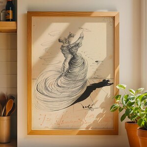 May include: A framed black and white print of a surrealist drawing hangs on a wall. The artwork depicts a figure with a flowing dress and a long shadow. The print is in a light wood frame. Two potted plants sit on a nearby counter.
