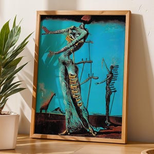 May include: A framed print of a surrealist artwork featuring a figure with outstretched arms, set against a turquoise background. The artwork has a wooden frame and is displayed on a wooden table, with a potted plant to the left.