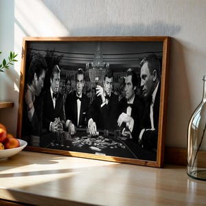 Peut inclure: Photographie en noir et blanc encadrée d'une scène de jeu de poker. Plusieurs hommes en smoking sont assis autour d'une table, avec des jetons et des cartes visibles. L'image est dans un cadre en bois, éclairée par un lustre.