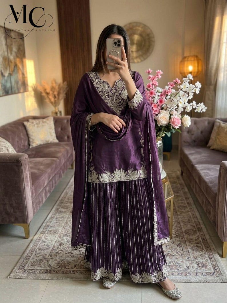 Może przedstawiać: Głęboki fioletowy zestaw salwar kameez z misternym srebrnym haftem na dekolcie, rękawach i obszyciu. Zestaw zawiera pasującą dupattę i spodnie z szerokimi nogawkami. Str&oacute;j wykonany jest z błyszczącej tkaniny.