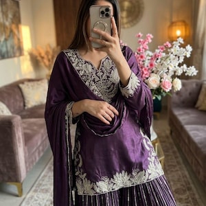 Może przedstawiać: Głęboki fioletowy, haftowany zestaw, składający się z tuniki, spodni z szerokimi nogawkami i pasującego szalika. Str&oacute;j ma skomplikowane srebrne hafty wok&oacute;ł dekoltu, rękaw&oacute;w i dołu. Widoczne jest logo marki "MC MIRZAYAA CLOTHING".