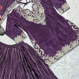 Może przedstawiać: Śliwkowy, trzyczęściowy str&oacute;j składający się z tuniki, sp&oacute;dnicy i szalika. Tunika ma skomplikowane srebrne hafty wok&oacute;ł dekoltu, rękaw&oacute;w i dołu. Sp&oacute;dnica jest plisowana z pionowymi srebrnymi paskami. Szalik r&oacute;wnież ma srebrne hafty.