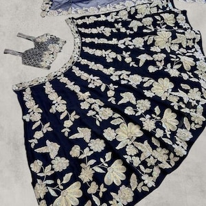 May include: A navy blue embroidered garment set with silver and white floral designs. The set includes a matching headpiece and a sheer, navy blue scarf with silver edging. The bottom right corner of the image displays the text "MC MIRZAYAA CLOTHING".