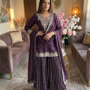 Może przedstawiać: Śliwkowy zestaw salwar kameez z misternym srebrnym haftem. Zestaw zawiera tunikę z długim rękawem, spodnie z szerokimi nogawkami i pasujący szal. Str&oacute;j jest ozdobiony szczeg&oacute;łową srebrną nicią wzdłuż dekoltu, mankiet&oacute;w i dołu.