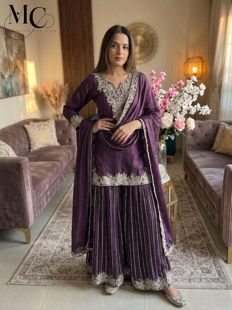 Może przedstawiać: Śliwkowy zestaw salwar kameez z misternym srebrnym haftem. Zestaw zawiera tunikę z długim rękawem, spodnie z szerokimi nogawkami i pasujący szal. Str&oacute;j jest ozdobiony szczeg&oacute;łową srebrną nicią wzdłuż dekoltu, mankiet&oacute;w i dołu.