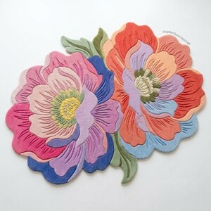 K&ouml;nnte beinhalten: Zwei florale Teppiche in einer lebendigen Farbpalette. Der eine Teppich hat rosa, lila und blaue Farbt&ouml;ne, w&auml;hrend der andere orange, pfirsichfarbene und blaue T&ouml;ne aufweist. Die Teppiche haben detaillierte Bl&uuml;tenblatt- und Blattdesigns.