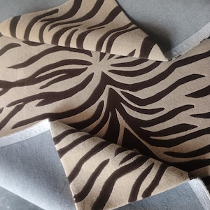 May include: Close-up of a tan and brown zebra print fabric. The fabric is folded over, revealing a light blue backing. The zebra stripes are dark brown and create a bold pattern. The fabric appears to be soft and textured.