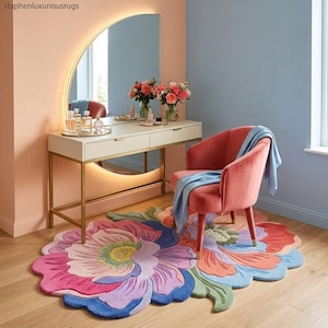 K&ouml;nnte beinhalten: Ein farbenfroher, bl&uuml;tenf&ouml;rmiger Teppich in Rosa, Blau und Gr&uuml;n dominiert den Vordergrund. Im Hintergrund befindet sich ein Schminktisch mit goldenem Rahmen und passendem Spiegel. Ein rosa Stuhl mit einem blauen &Uuml;berwurf rundet die Szene ab.
