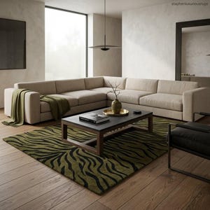 Puede incluir: Salón moderno con un gran sofá esquinero beige, una mesa de centro de madera oscura y una alfombra con estampado de cebra verde y negro. Una manta verde y un jarrón decorativo añaden color al espacio neutro. La habitación tiene una ventana grande y un diseño minimalista.
